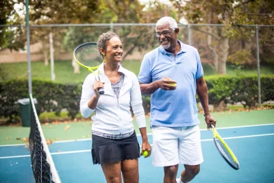 Two adults, walking off of the tennis court, talking to each other and having a great time.