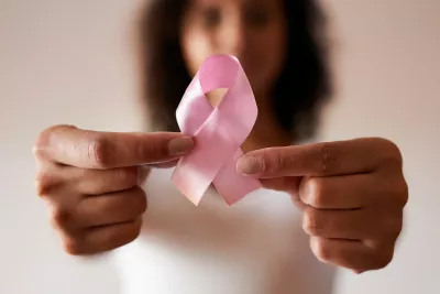 Woman holding a pink ribbon out in front of her, showing her support for Breast Cancer Awareness Month.