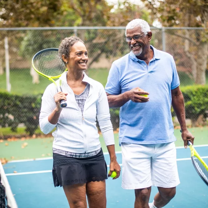 Two adults, walking off of the tennis court, talking to each other and having a great time.