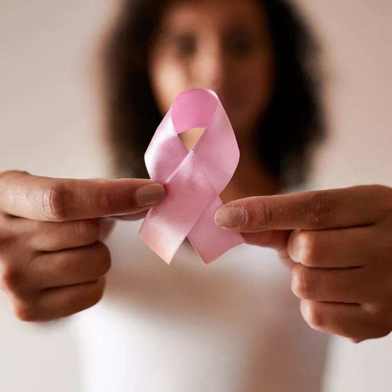 Woman holding a pink ribbon out in front of her, showing her support for Breast Cancer Awareness Month.