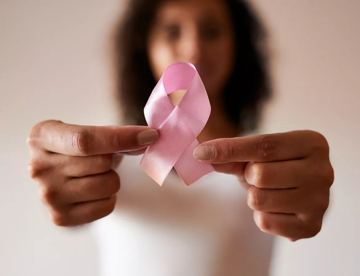 Woman holding a pink ribbon out in front of her, showing her support for Breast Cancer Awareness Month.